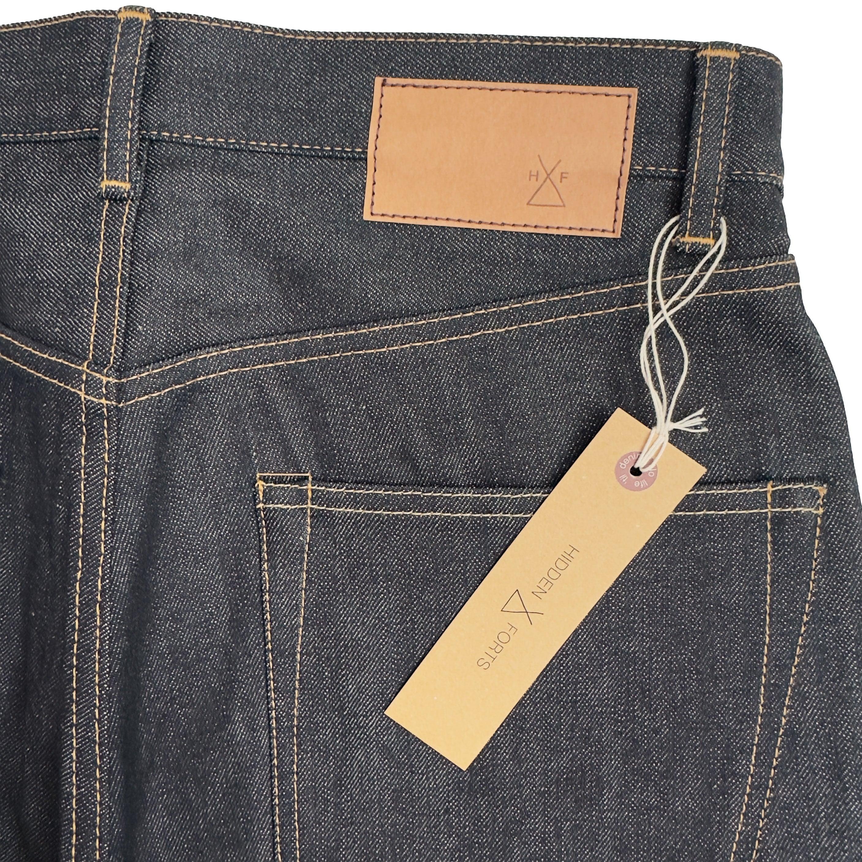 Closeup of the HFD-01 jacron patch and kraft paper hangtag with logo on Japanese selvedge denim relaxed fit wide leg jeans.