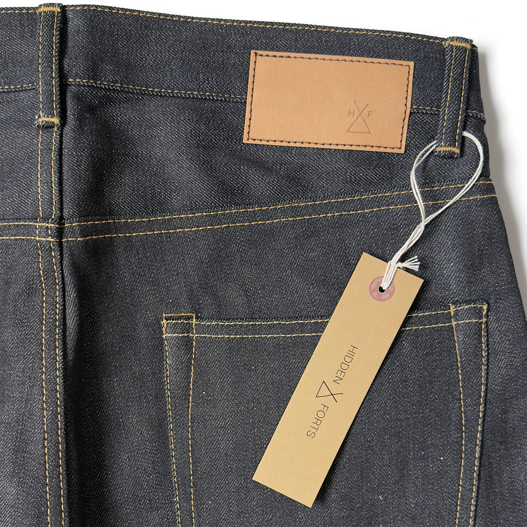 Closeup of the HFD02 jacron paper patch and kraft paper hangtag with logo on Japanese selvedge denim relaxed fit tight tapered leg jeans.