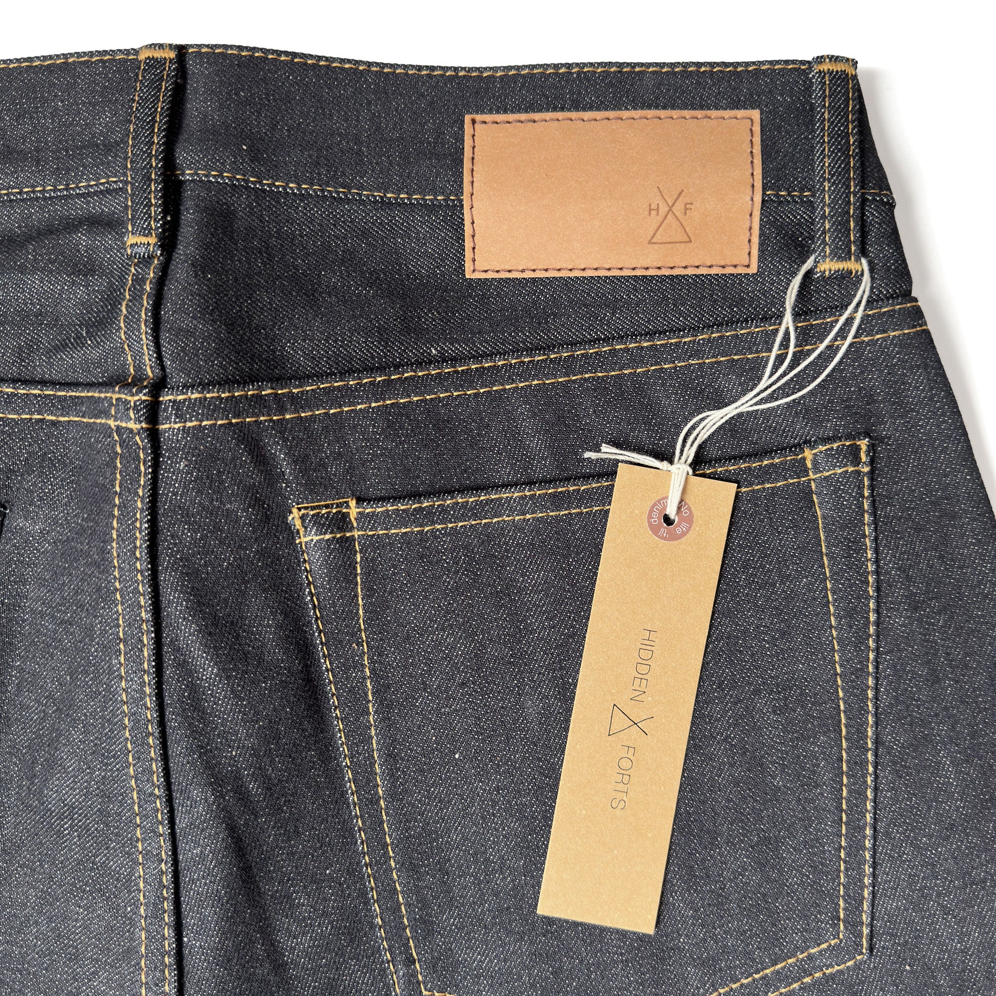 Closeup of the HFD04 jacron paper patch and kraft paper hangtag with logo on Japanese selvedge denim slim fit straight leg jeans.