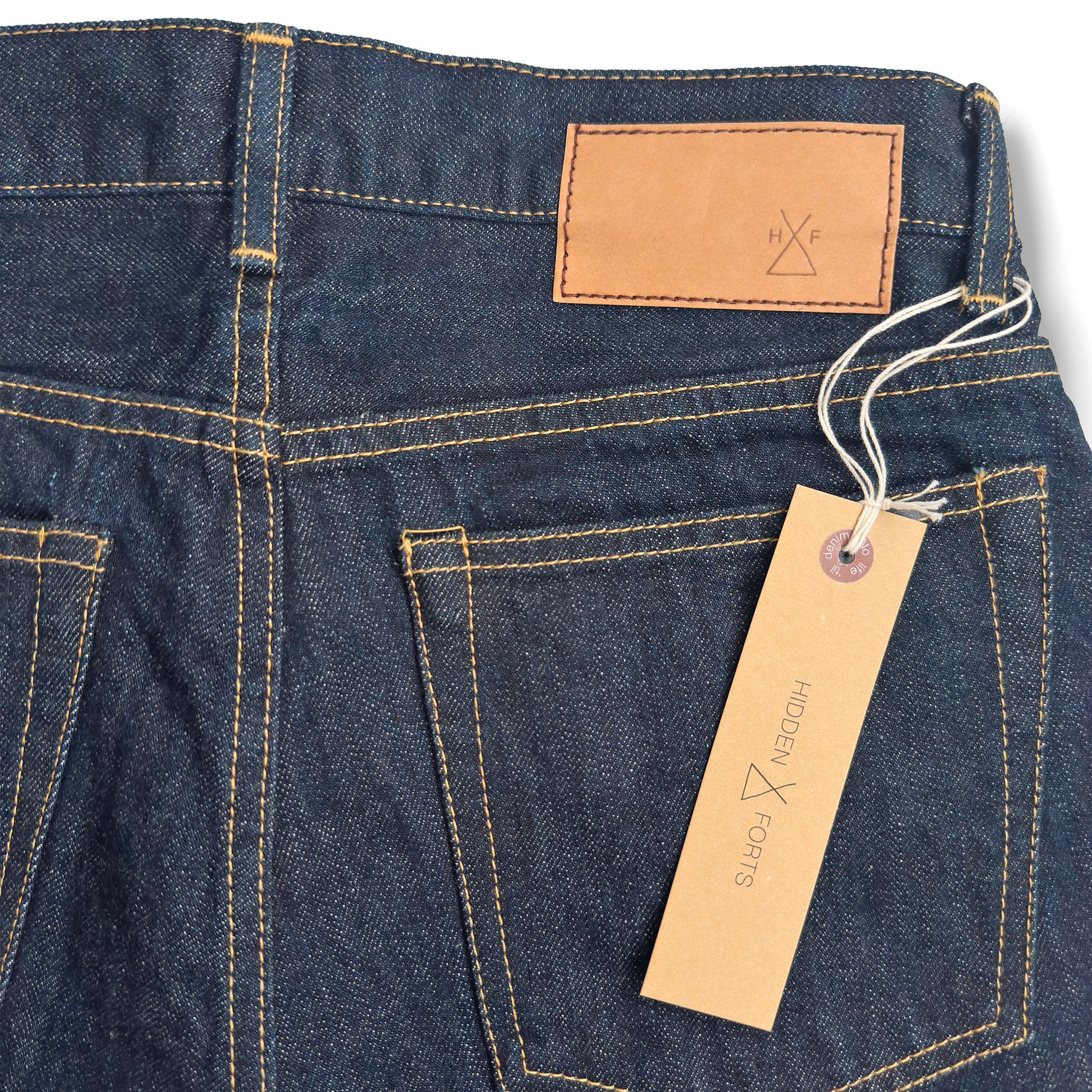 Closeup of the HFD-04W jacron paper patch and kraft paper hangtag with logo on Japanese selvedge denim once washed slim fit straight leg jeans.